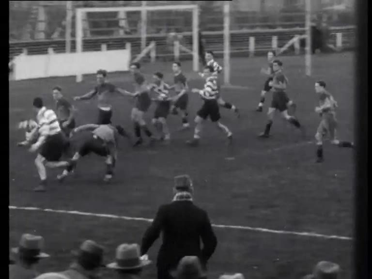 Black-and-white newsreel frame of AAC and AVRC rugby players contesting possession after a scrum in Amsterdam in 1933.