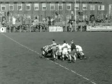 Black-and-white wide view of AAC in broad-banded shirts and Bank of England in pale shirts contesting a scrum in Amsterdam in April 1955, with spectators behind the far touchline.