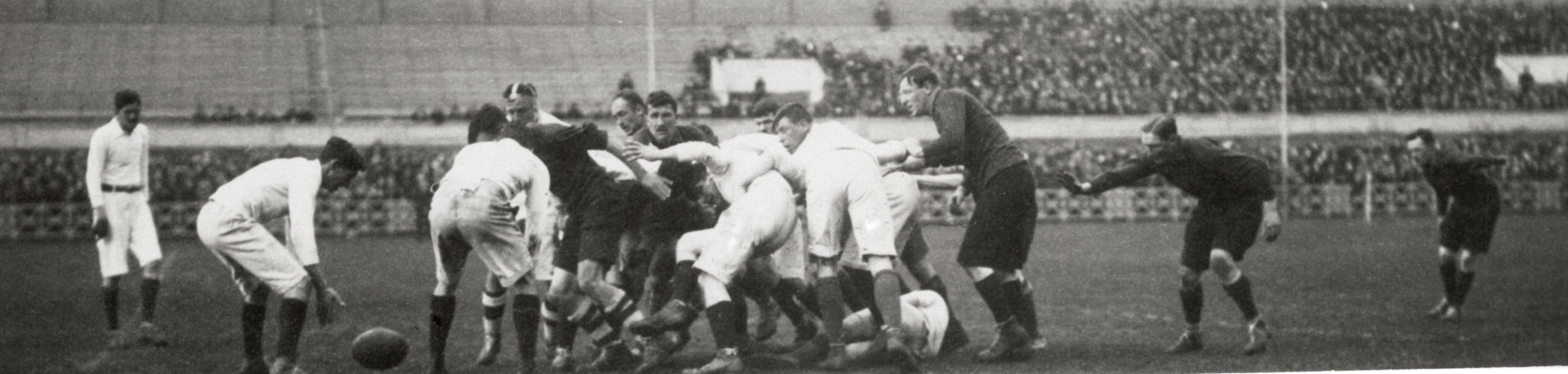 Wide black-and-white photograph from 1918 of two teams of British internees forming a rugby scrum at Stadion Amsterdam, with spectators behind them.