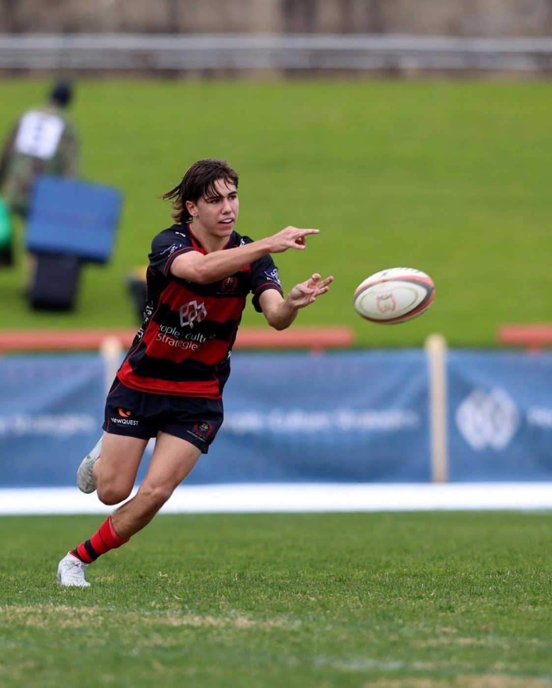 Frankie Dunkin fires a long pass across the field in red-and-black hooped club kit