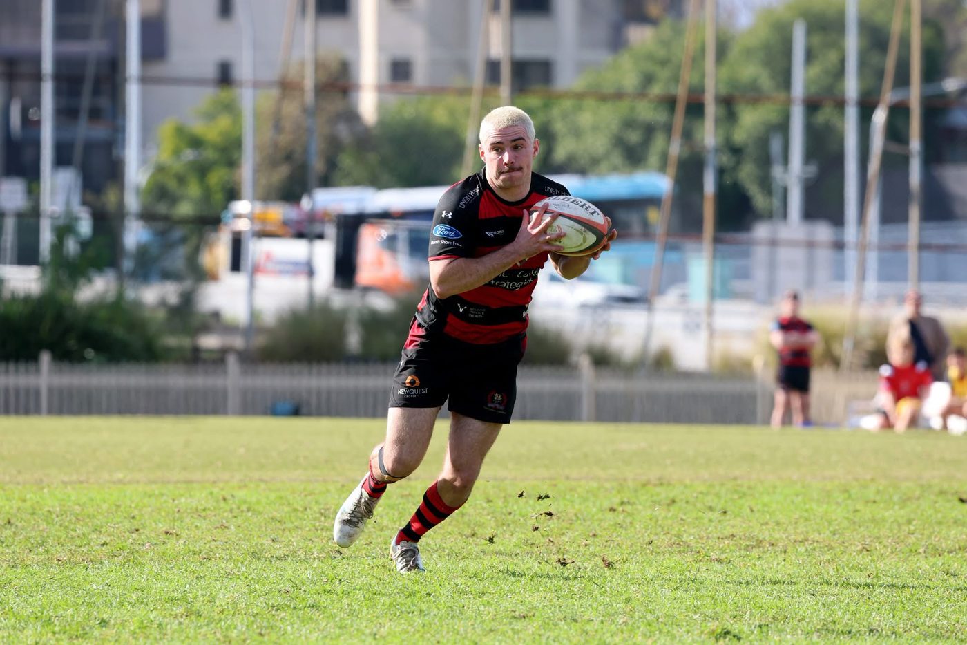 Harry White runs onto the ball in open play, wearing red-and-black hooped club kit