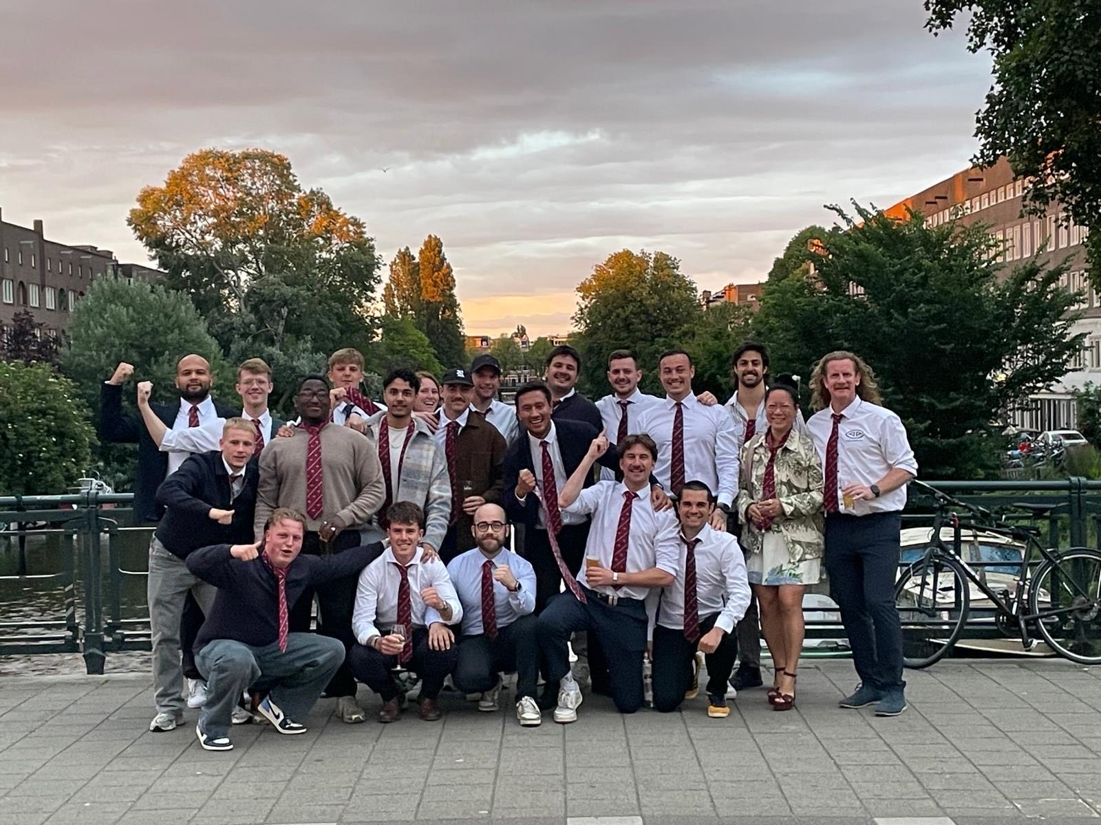 The men's 2nd XV squad in white shirts and red ties celebrate their promotion on a canal bridge
