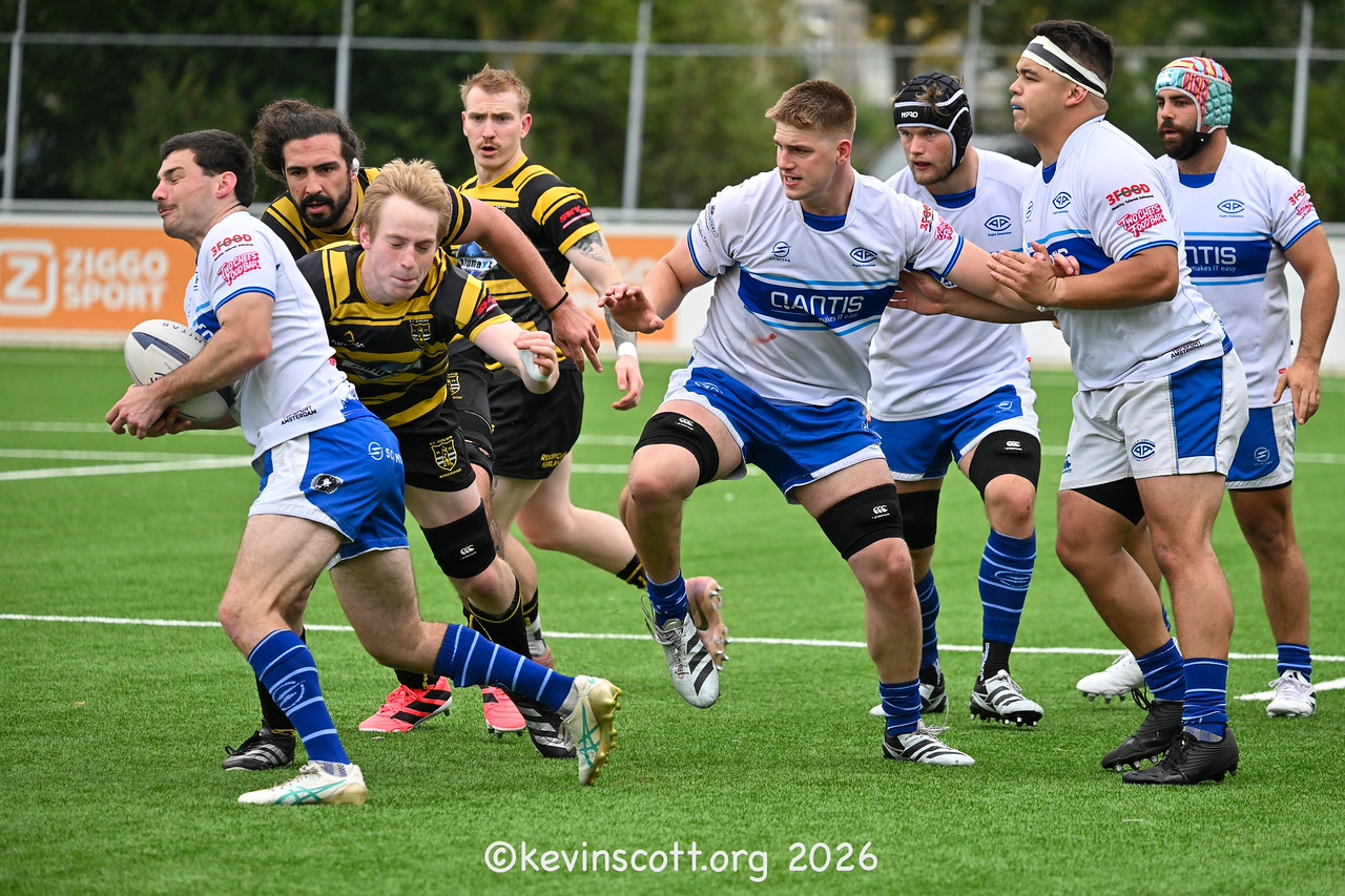 An AAC player in white-and-blue kit carries the ball against RC Eemland